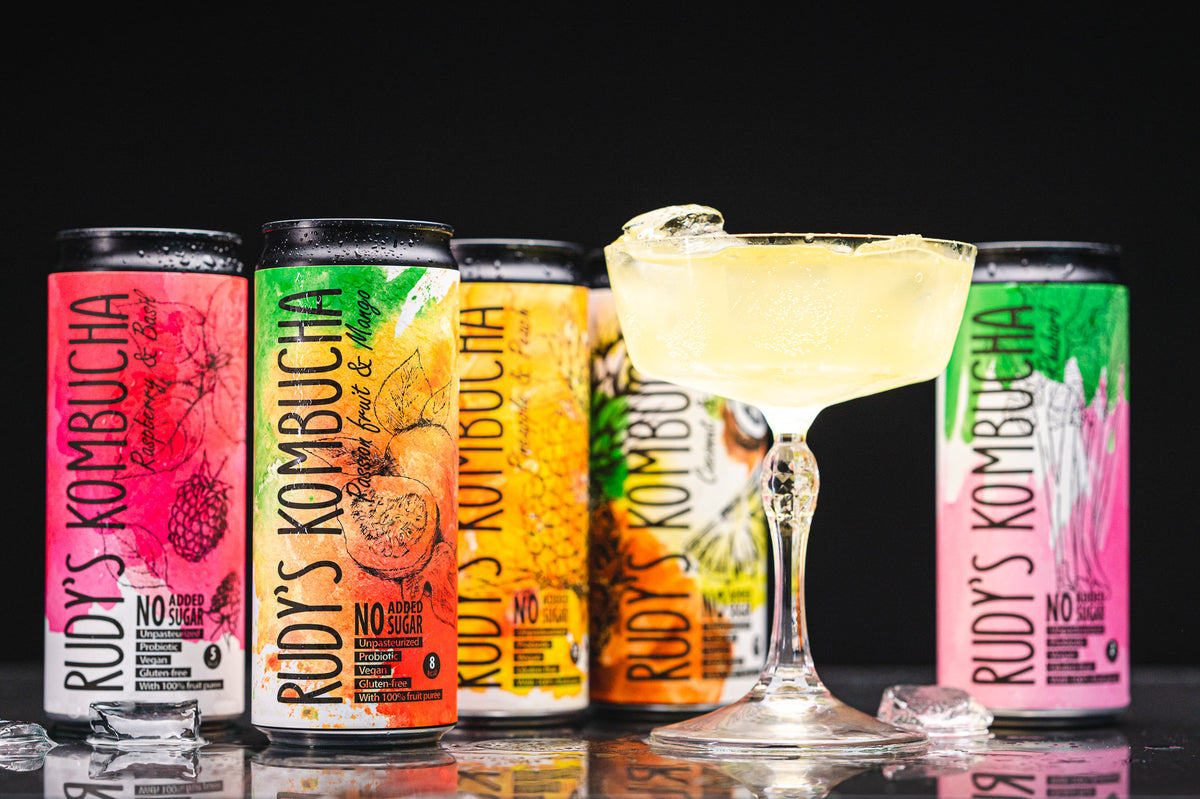 A row of Rudy's Kombucha cans beside a poured glass